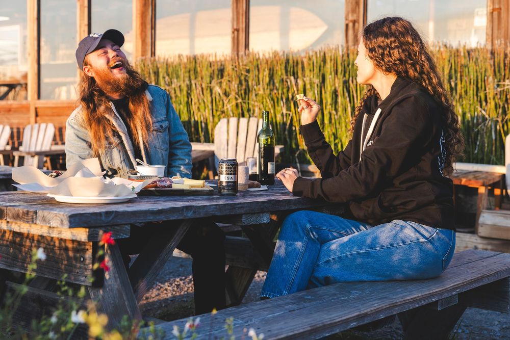 People relaxing at an outdoor restaurant with blue benches and tall grass in background.