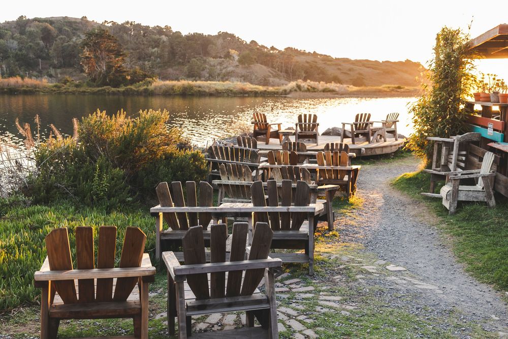 Wooden Adirondack chairs arranged along a waterfront path at sunset with warm evening light.