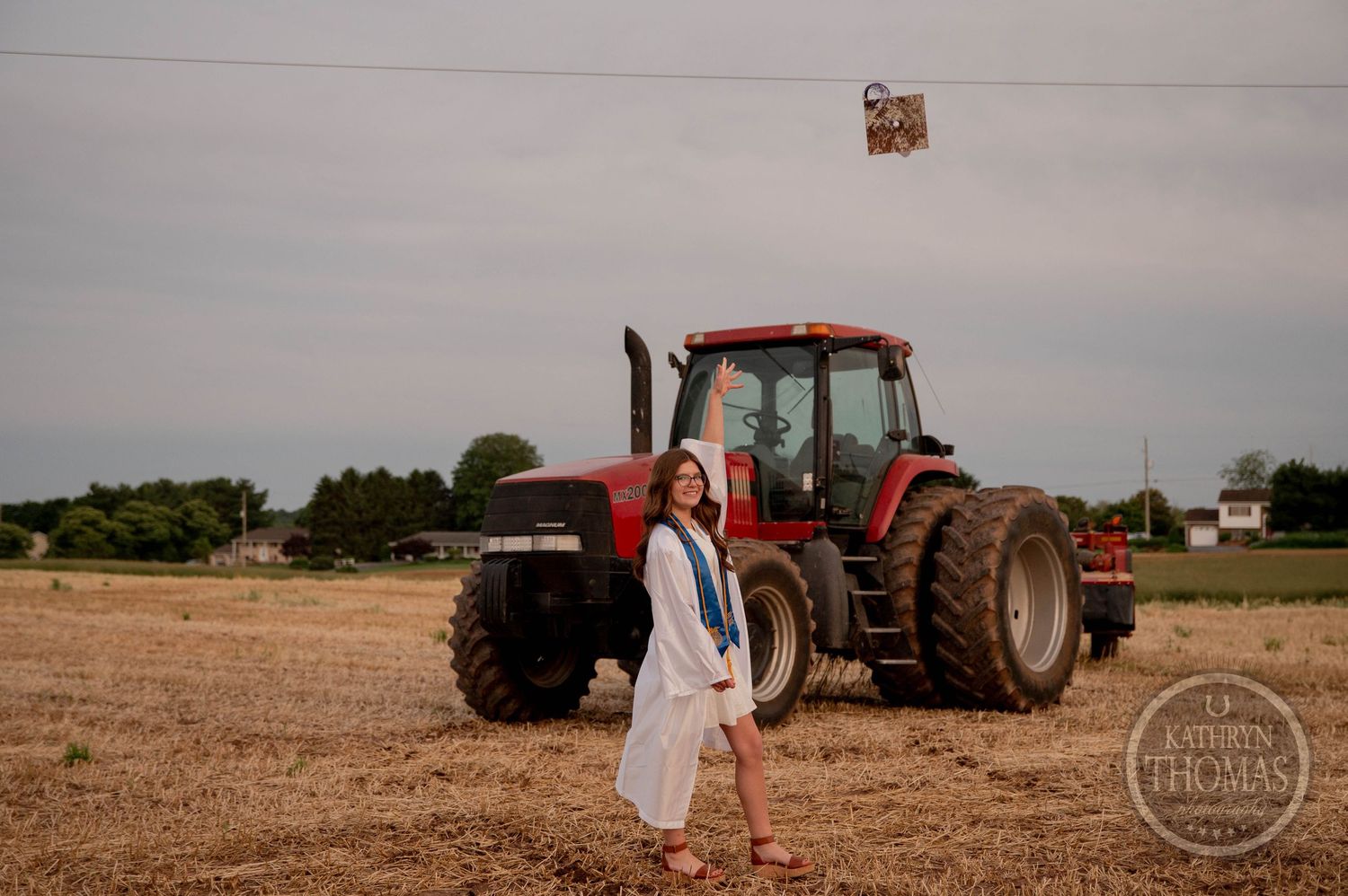 Red tractors and farming equipment dot the rural landscape as a couple leans against each other in golden agricultural fields.