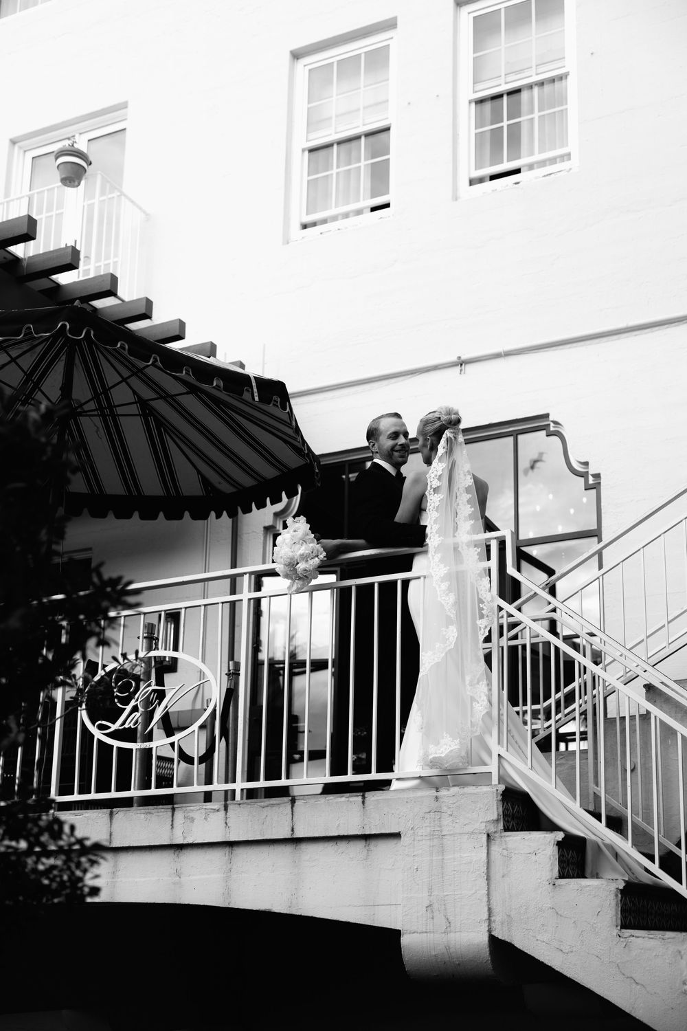 Black and white photo of a bride and groom sharing a romantic moment on an elegant venue balcony on their wedding day.