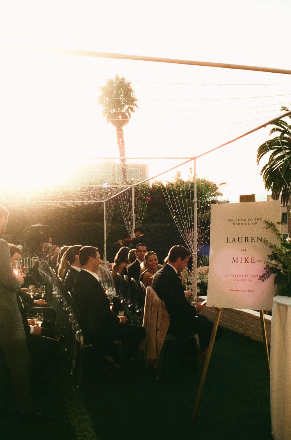 Outdoor wedding reception at golden hour with guests mingling near a welcome sign for Lauren and Mike.
