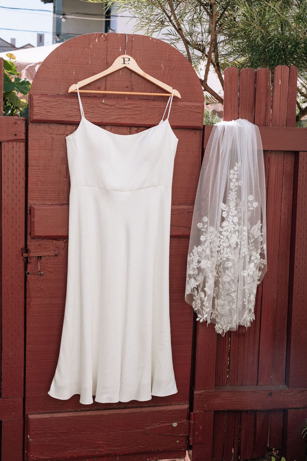 A short wedding dress hangs next to a wedding veil before ceremony
