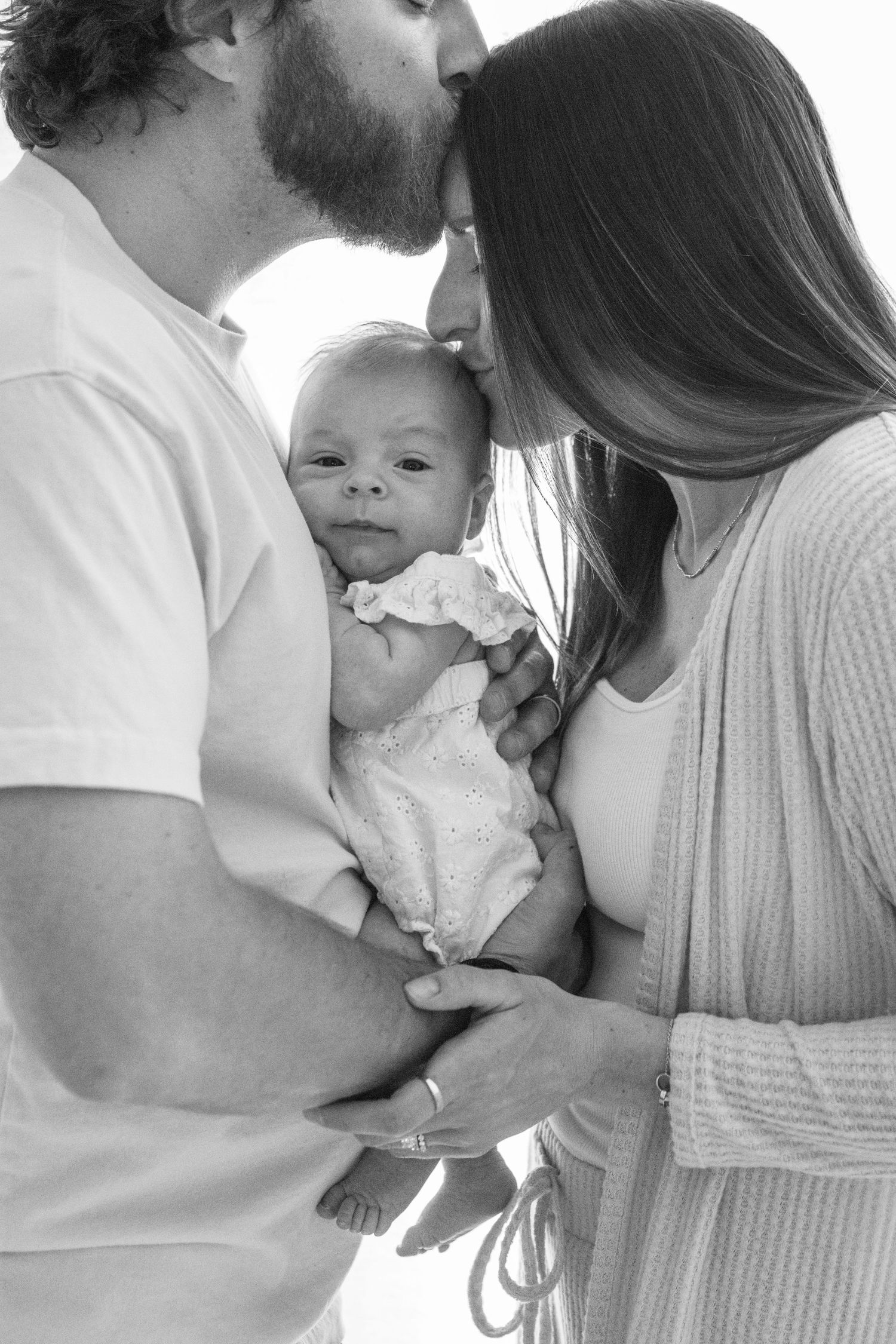 Black and white intimate family portrait showing tender moments with baby.