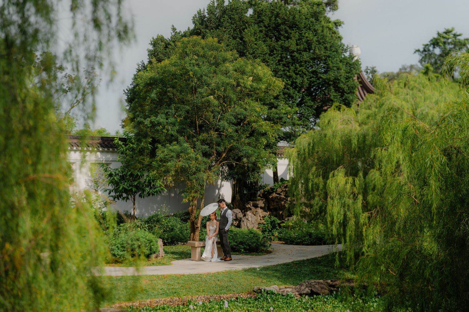 A scenic garden wedding path lined with willows and greenery leading to an intimate outdoor ceremony space.