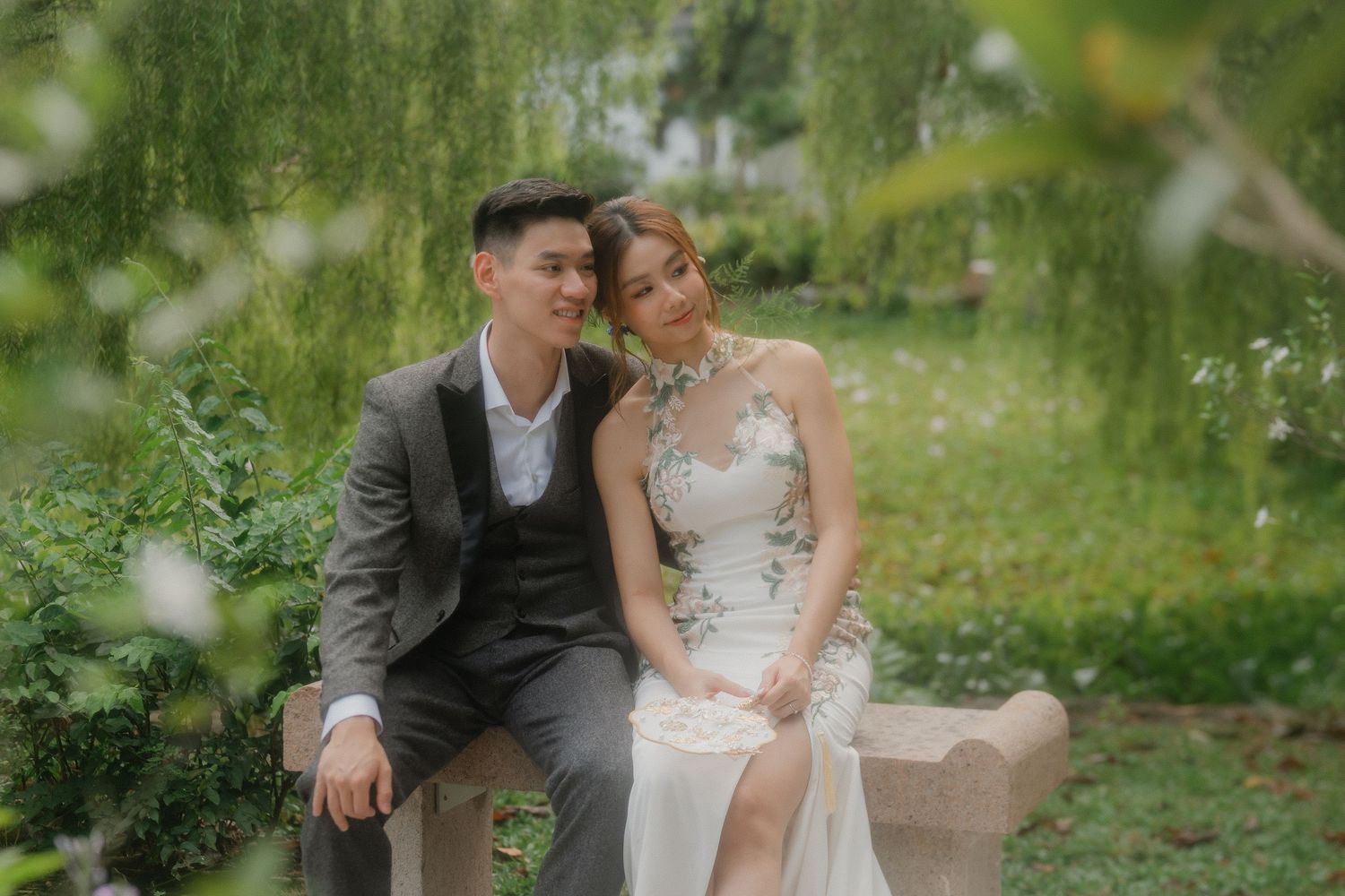 A romantic outdoor portrait of a couple in wedding attire sitting together in a lush garden setting.