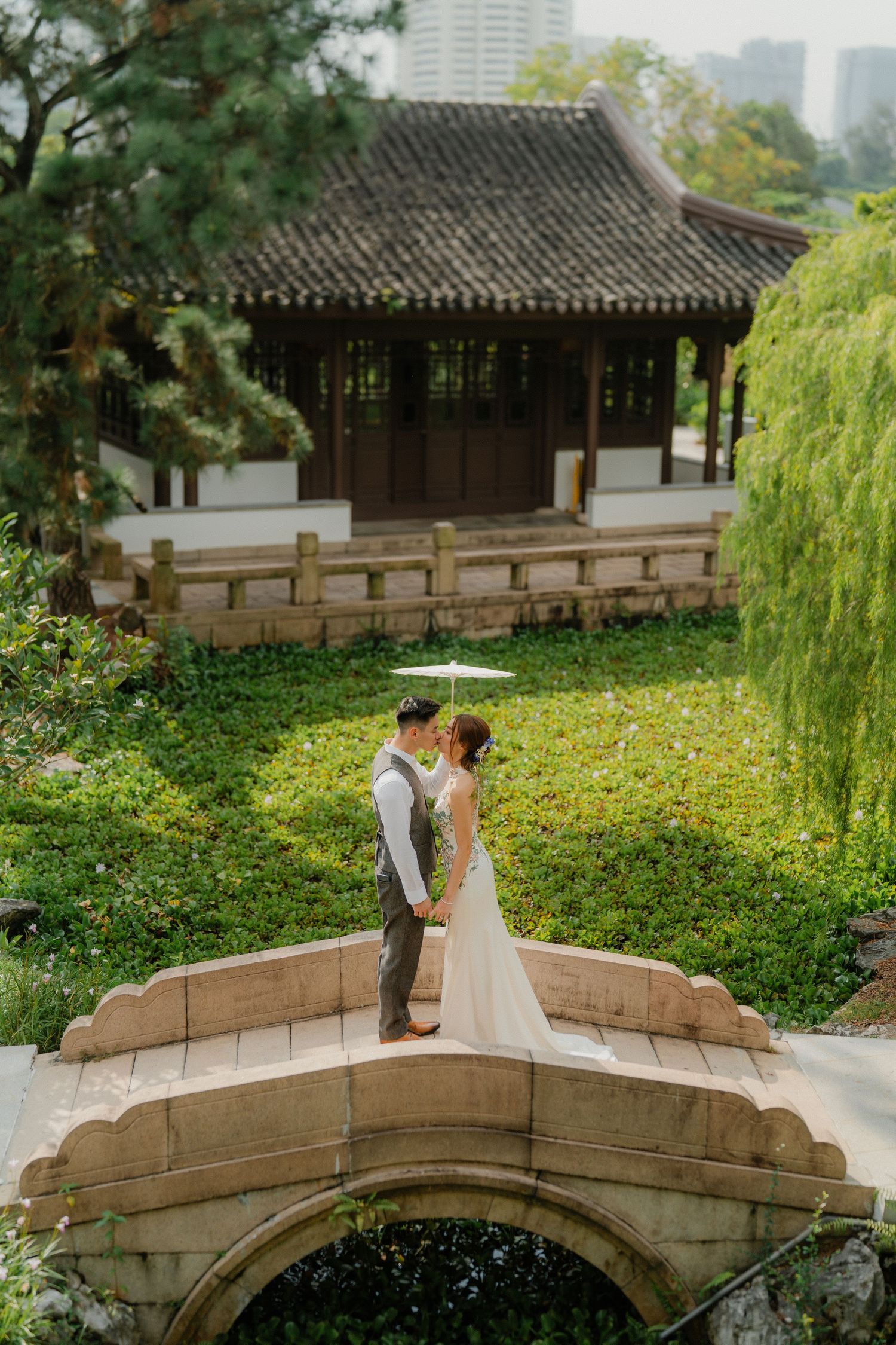A romantic wedding photo on a stone bridge with traditional Chinese architecture in the background.