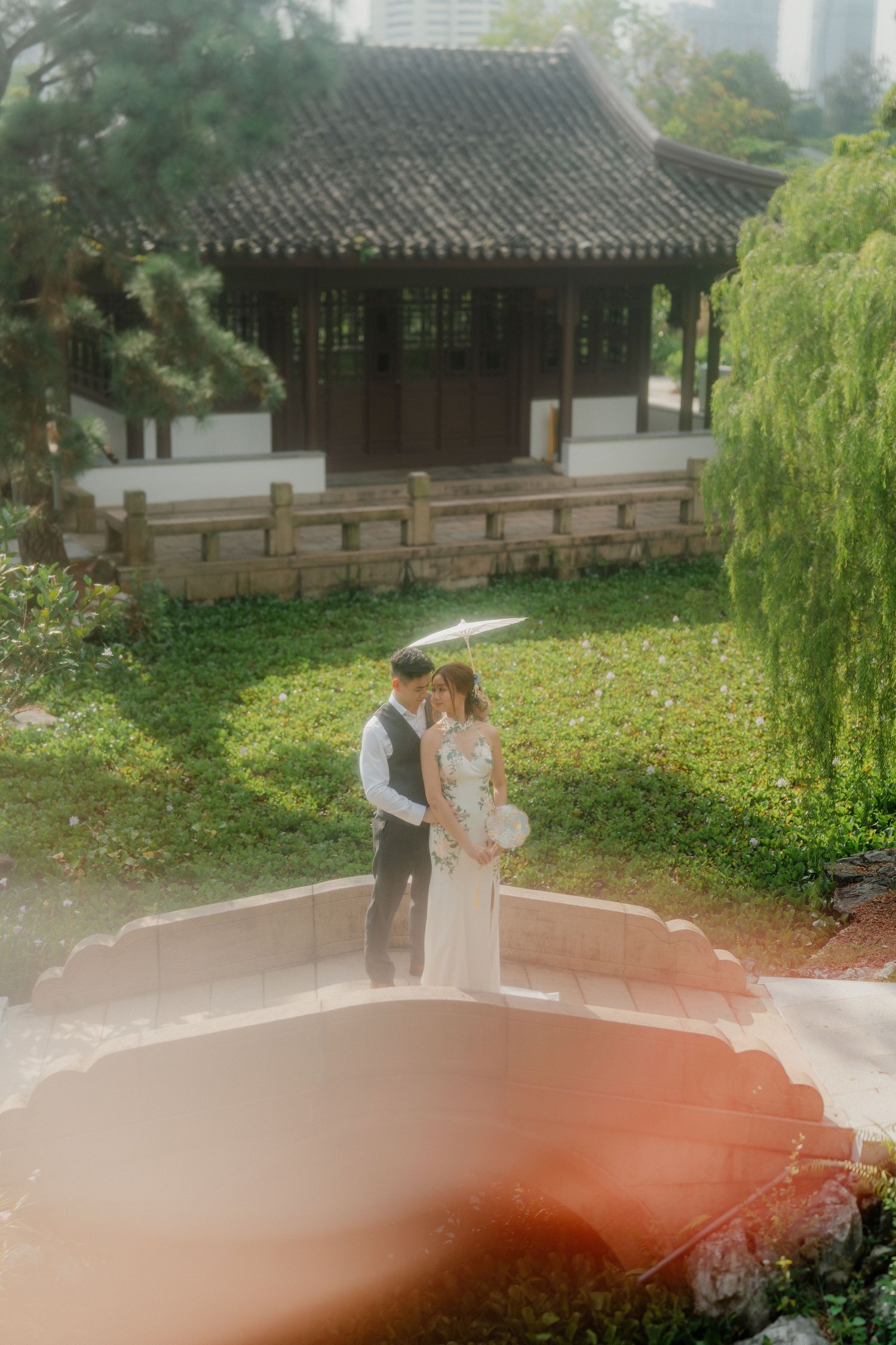 Newlyweds share an intimate moment on an arched bridge in a Chinese garden.
