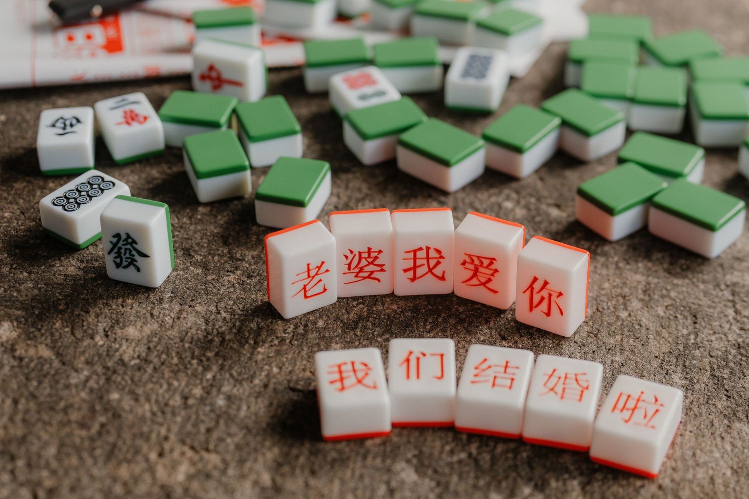 Chinese mahjong tiles arranged with red banners displaying Chinese characters on stone surface.