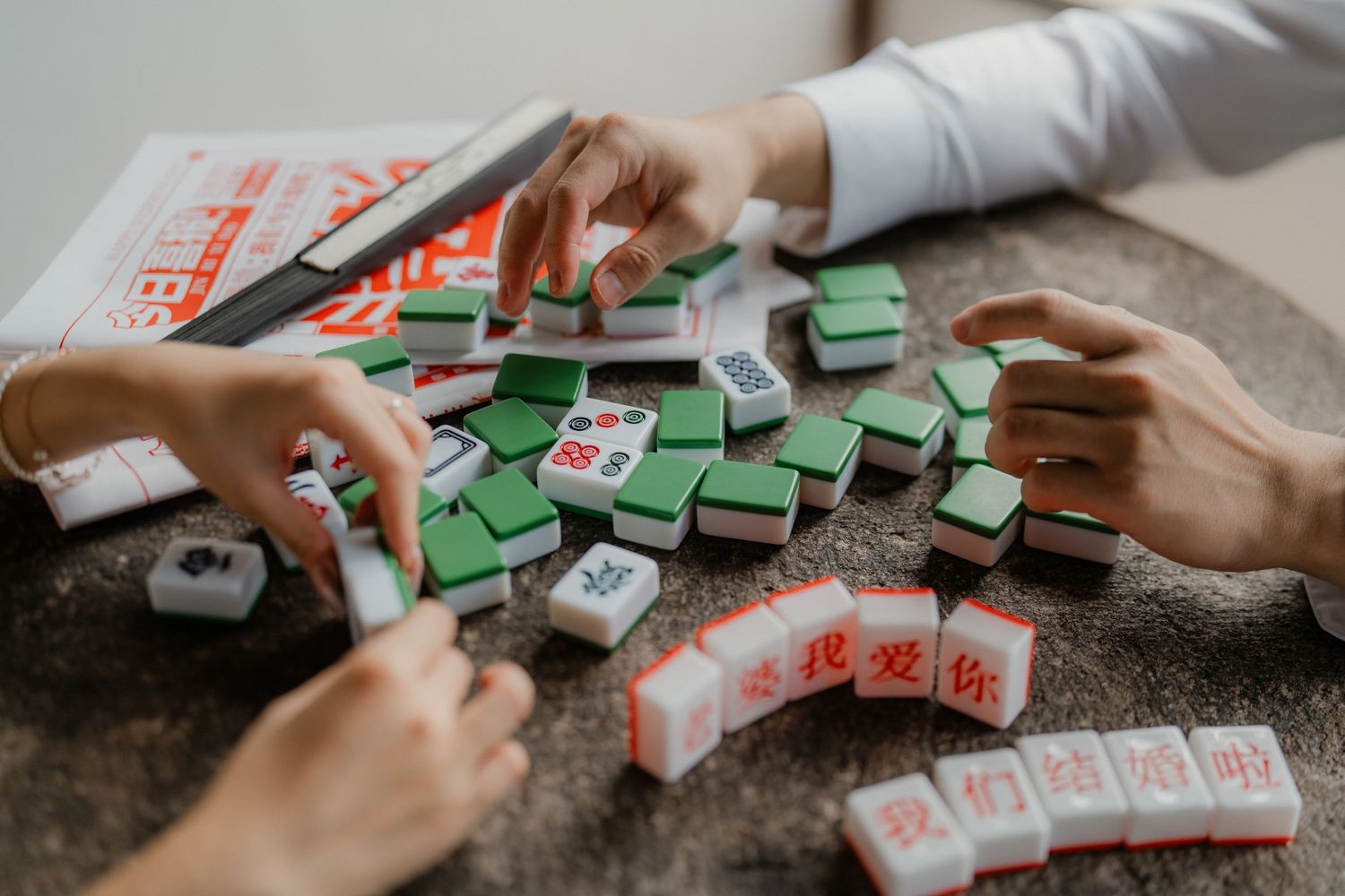 Mahjong tiles being arranged on a gray table to spell out Chinese characters.