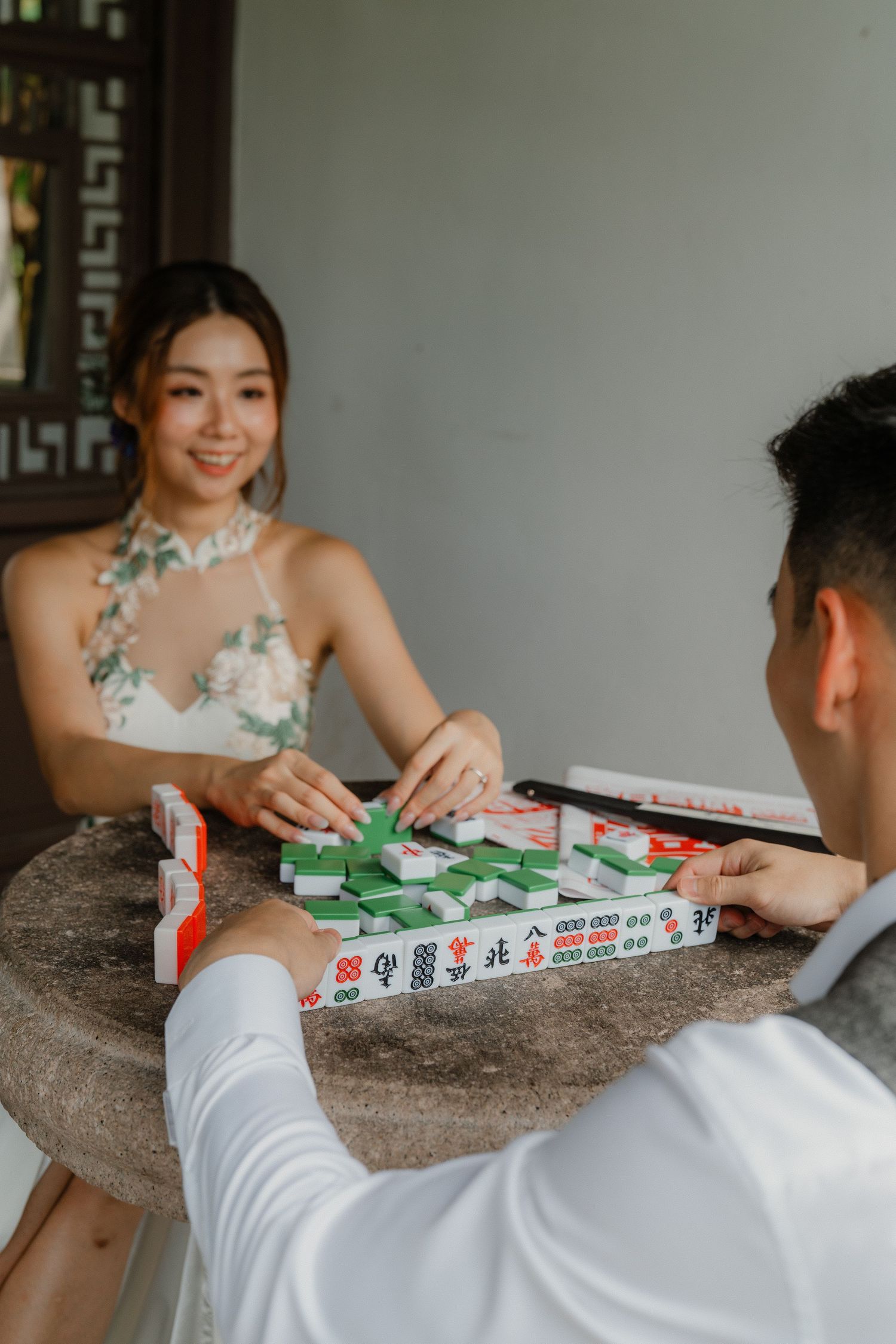Couple playing mahjong together at a table showcasing traditional Chinese game elements.