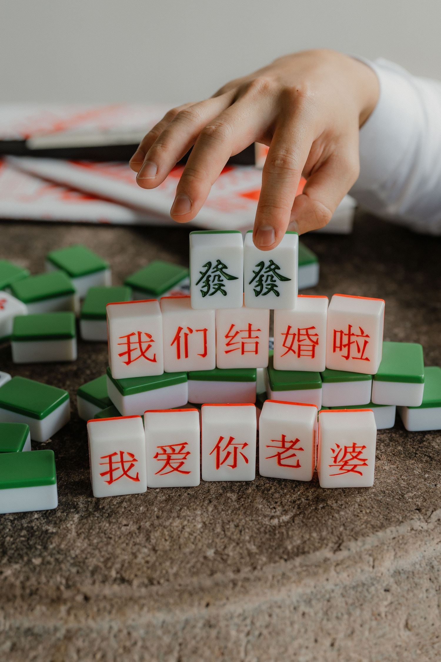 A hand arranges Chinese mahjong tiles spelling out wedding messages in Mandarin characters.