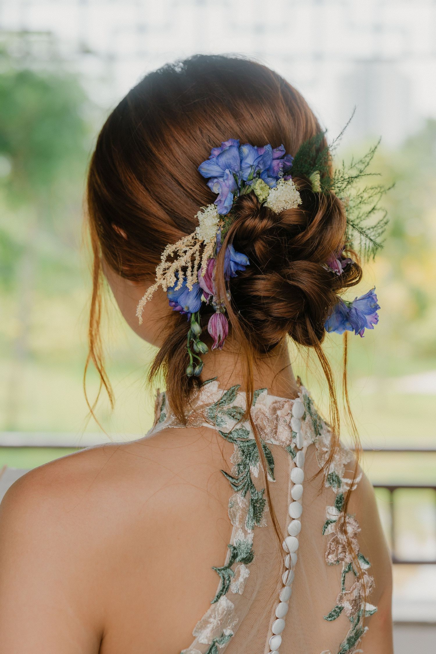 Delicate blue and purple flowers adorning an elegant updo hairstyle against a soft natural background.