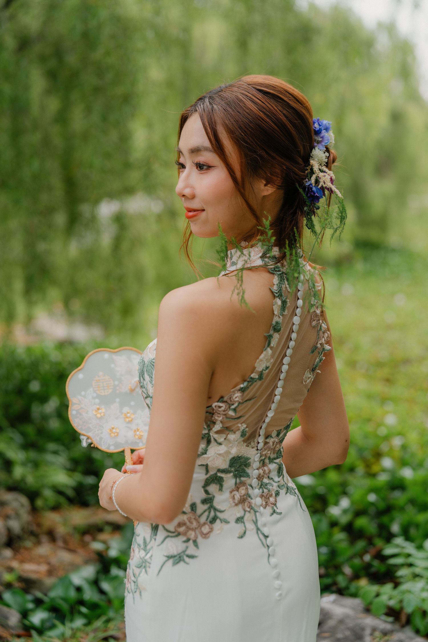 Bride in elegant white dress with floral embellishments poses in garden setting.