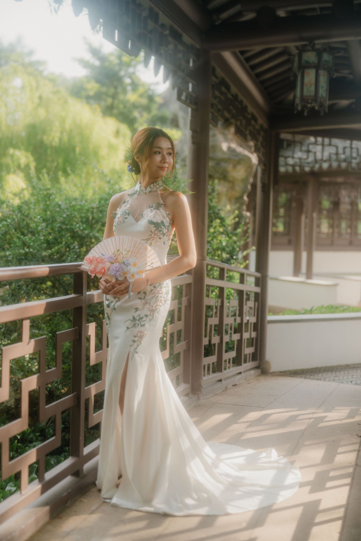An elegant white wedding dress with floral details photographed in a traditional Chinese garden pavilion.