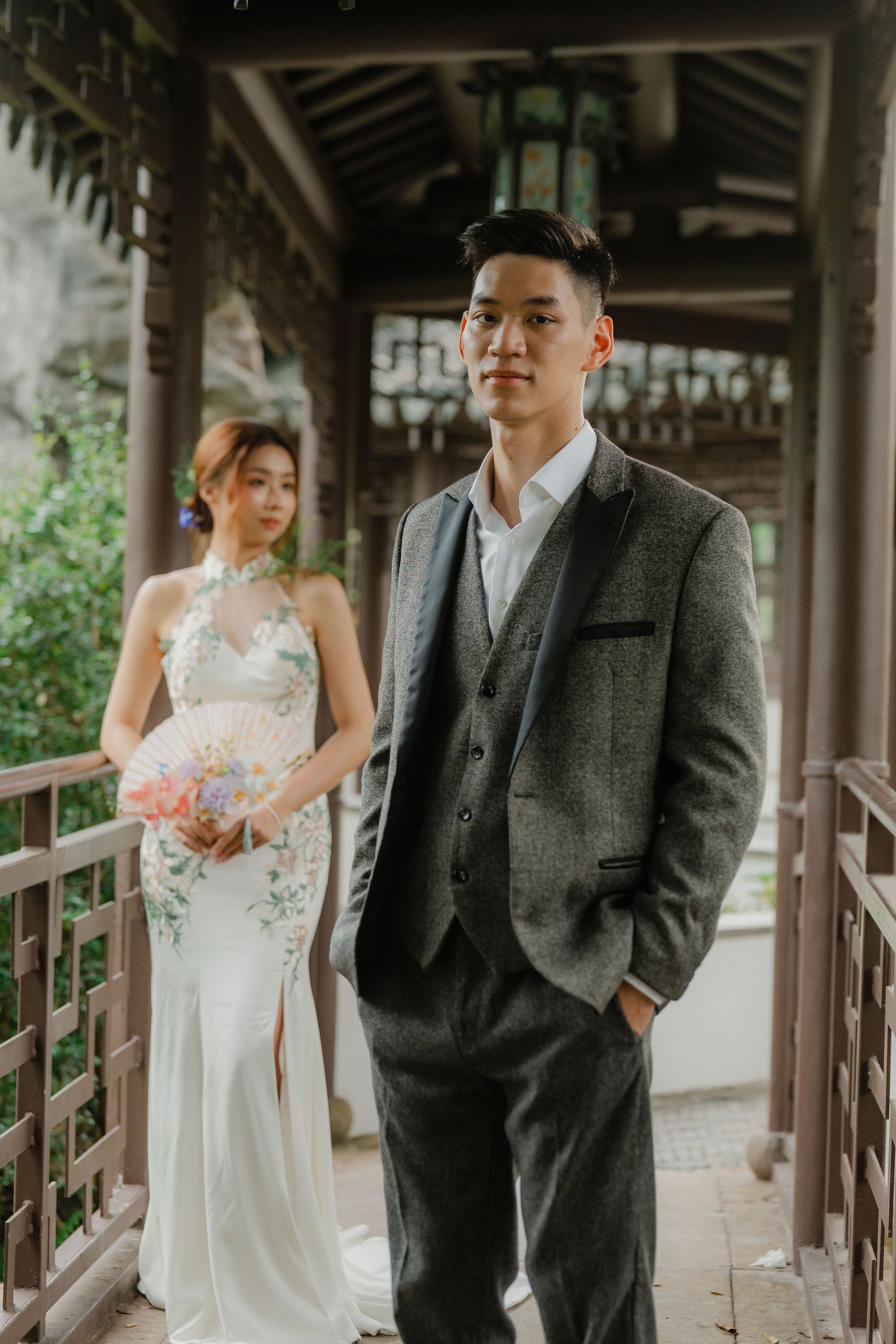 Couple in wedding attire standing in traditional Asian covered corridor.