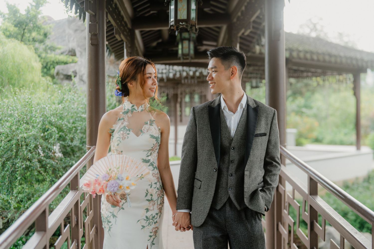 Newlyweds walking through traditional covered walkway surrounded by greenery.