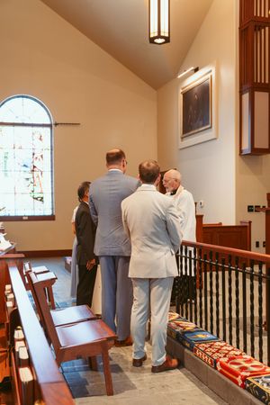 People in formal attire viewing displays along a carpeted hallway with wooden railings and pendant lighting.