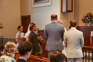Wedding party members gather near the altar in a church with wooden pews and traditional architecture.