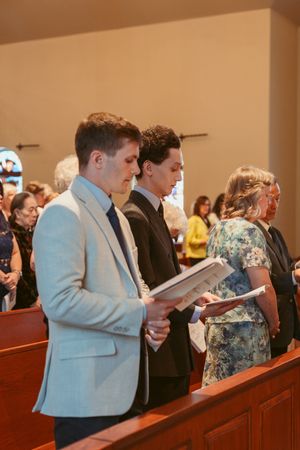 Young attendees in formal attire read from hymnals during a church service.