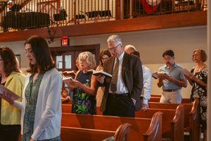 Church members follow along in their hymnals while standing in wooden pews during worship.