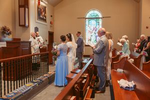 Wedding ceremony in progress with guests standing in church pews under arched windows.
