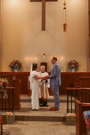 Wedding ceremony taking place at a church altar decorated with floral arrangements and candles.