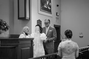 A black and white photograph capturing an intimate wedding ceremony moment inside a church.