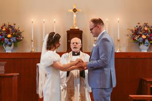 A traditional wedding ceremony takes place at the altar with lit candles and floral arrangements on either side.