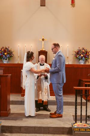 Wedding ceremony in a church with candles and floral arrangements as a couple exchanges rings at the altar.