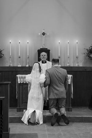 Black and white photo of a wedding ceremony in a church with a couple kneeling at the altar with seven lit candles.