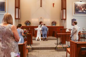 Intimate church wedding ceremony with white candles and floral arrangements at the altar.
