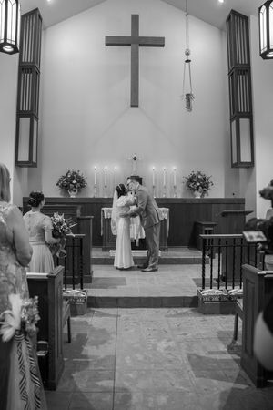 A romantic black and white church wedding ceremony with a cross on the wall, candles, and floral arrangements.