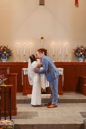 A wedding ceremony moment by candlelight with bright floral arrangements at a church altar.