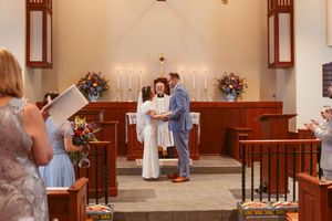 A wedding ceremony at the church altar with floral arrangements and lit candles in the background.