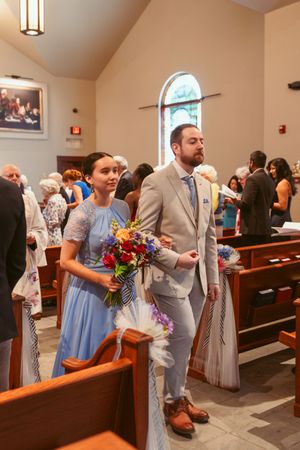Wedding party members in light blue and gray attire walking down the church aisle past wooden pews.