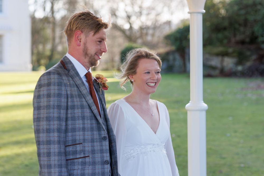 A newlywed couple shares a joyful moment together outdoors near a white column on their wedding day.