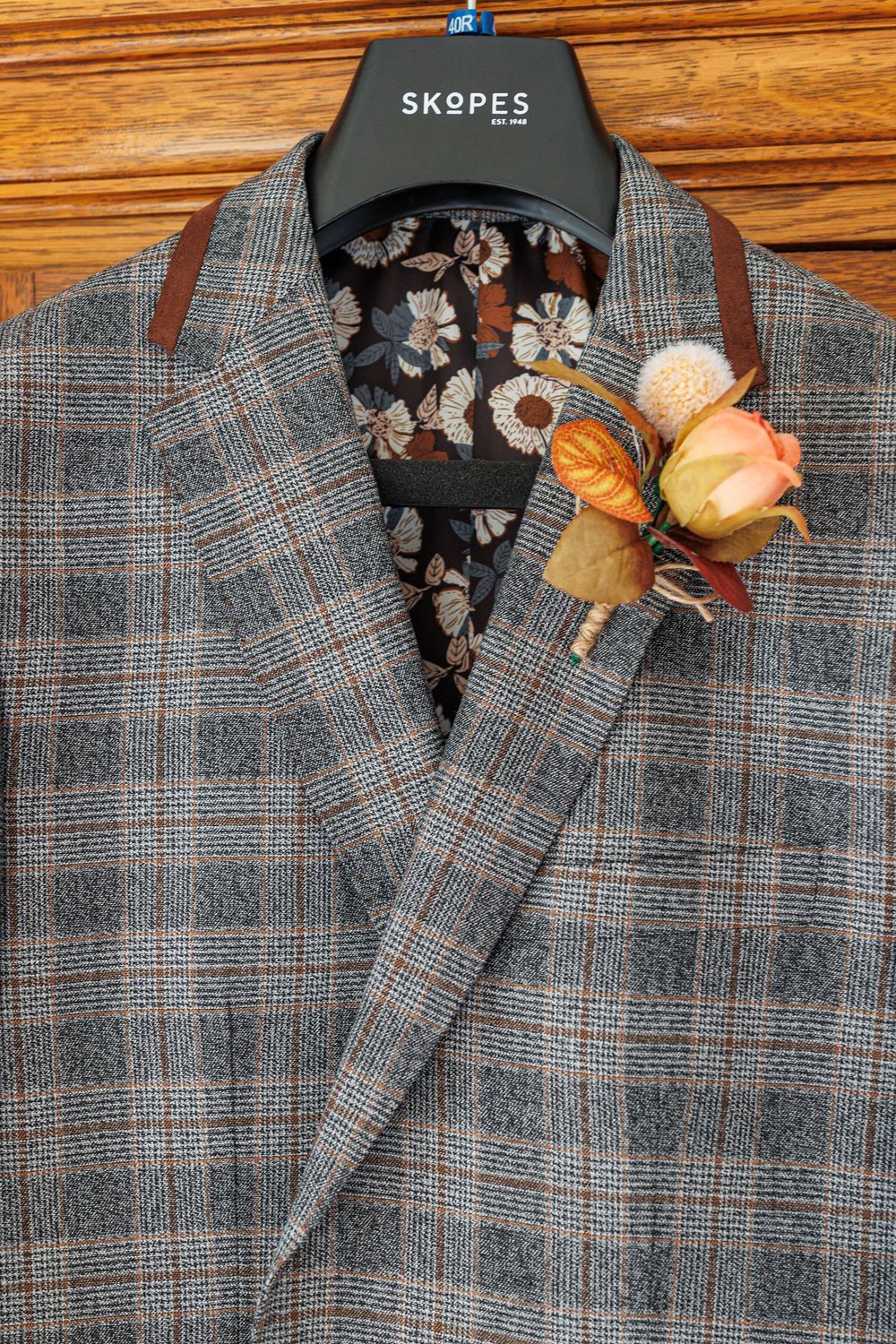 Gray plaid suit jacket on hanger decorated with dried orange and burgundy flowers.