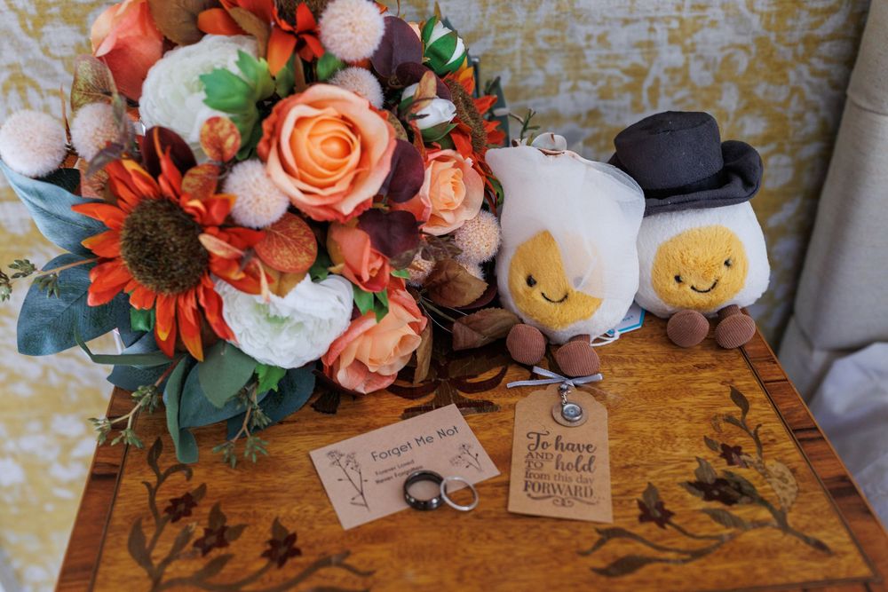 Colorful autumn-themed wedding floral arrangement with peach roses and orange daisies on wooden surface.