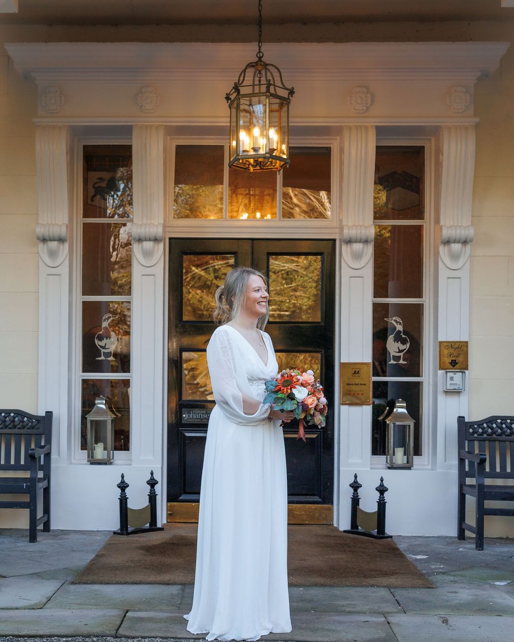 A figure in a flowing white wedding dress stands on an elegant porch with lantern lighting and white columns.