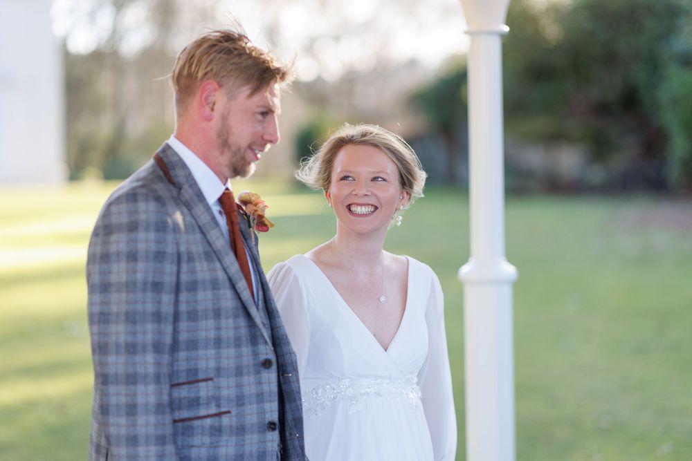Wedding couple smiles together on white porch during outdoor countryside celebration.
