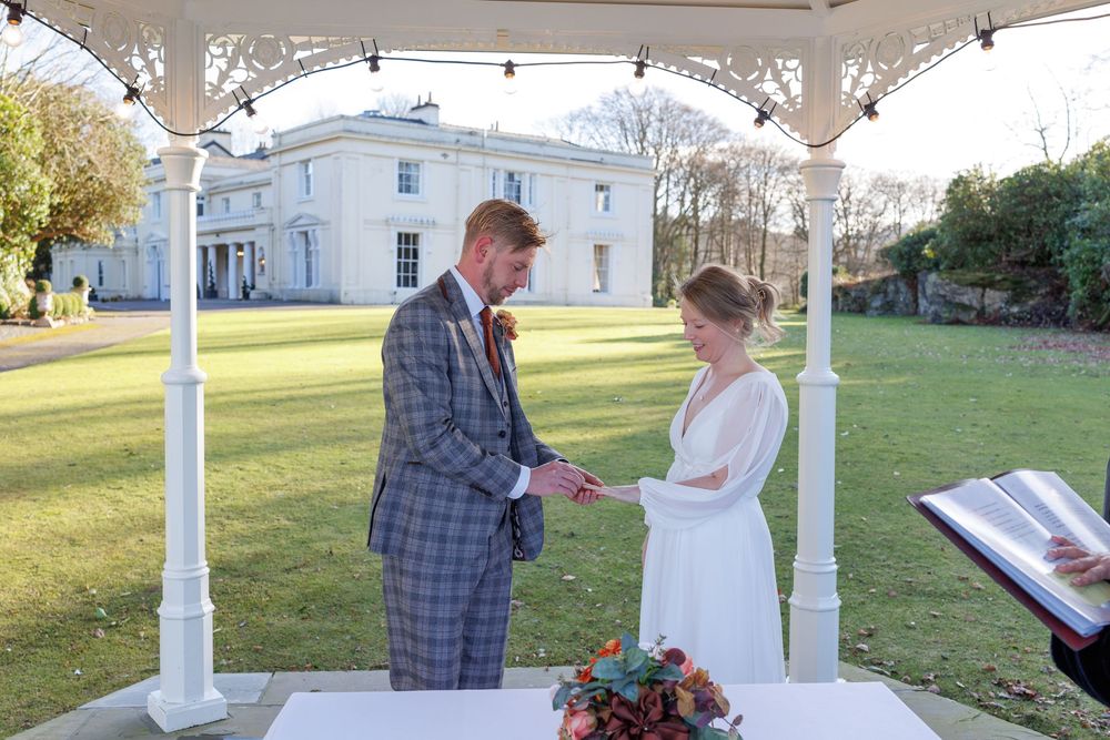 A wedding ceremony taking place under a white gazebo on a sunny day.