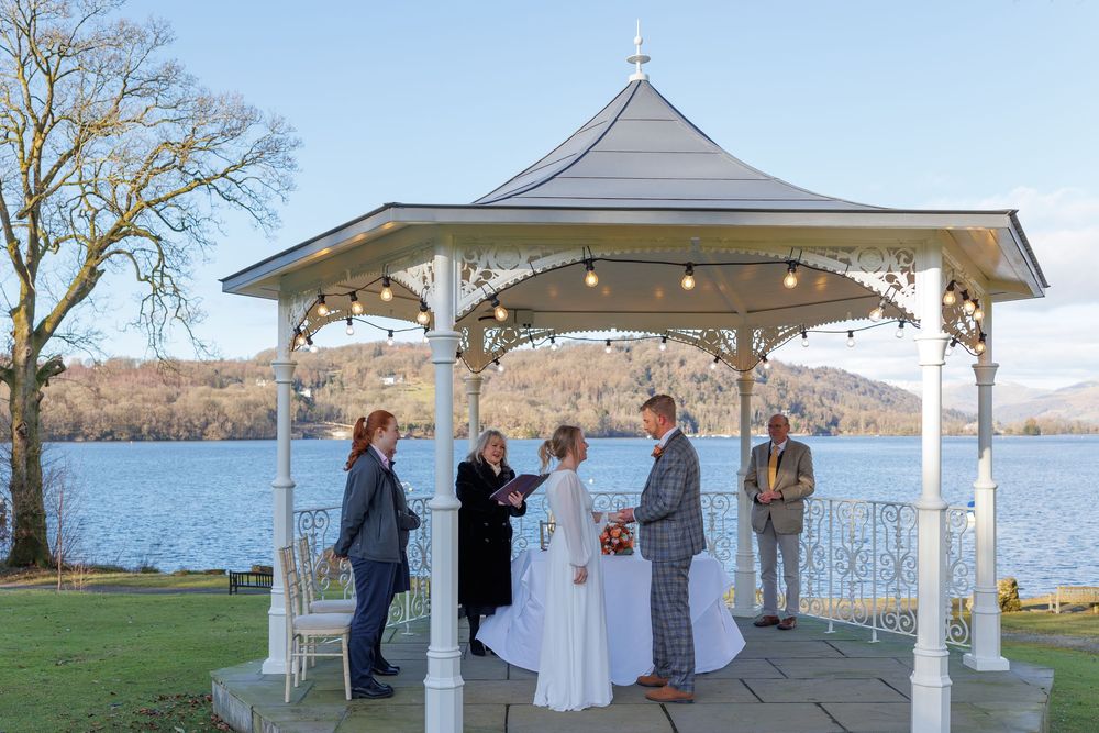 A waterfront wedding ceremony in a white gazebo with guests in attendance.
