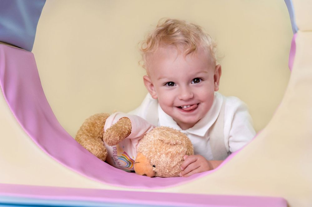 A young child plays peek-a-boo through holes in a plastic play structure at a playground.