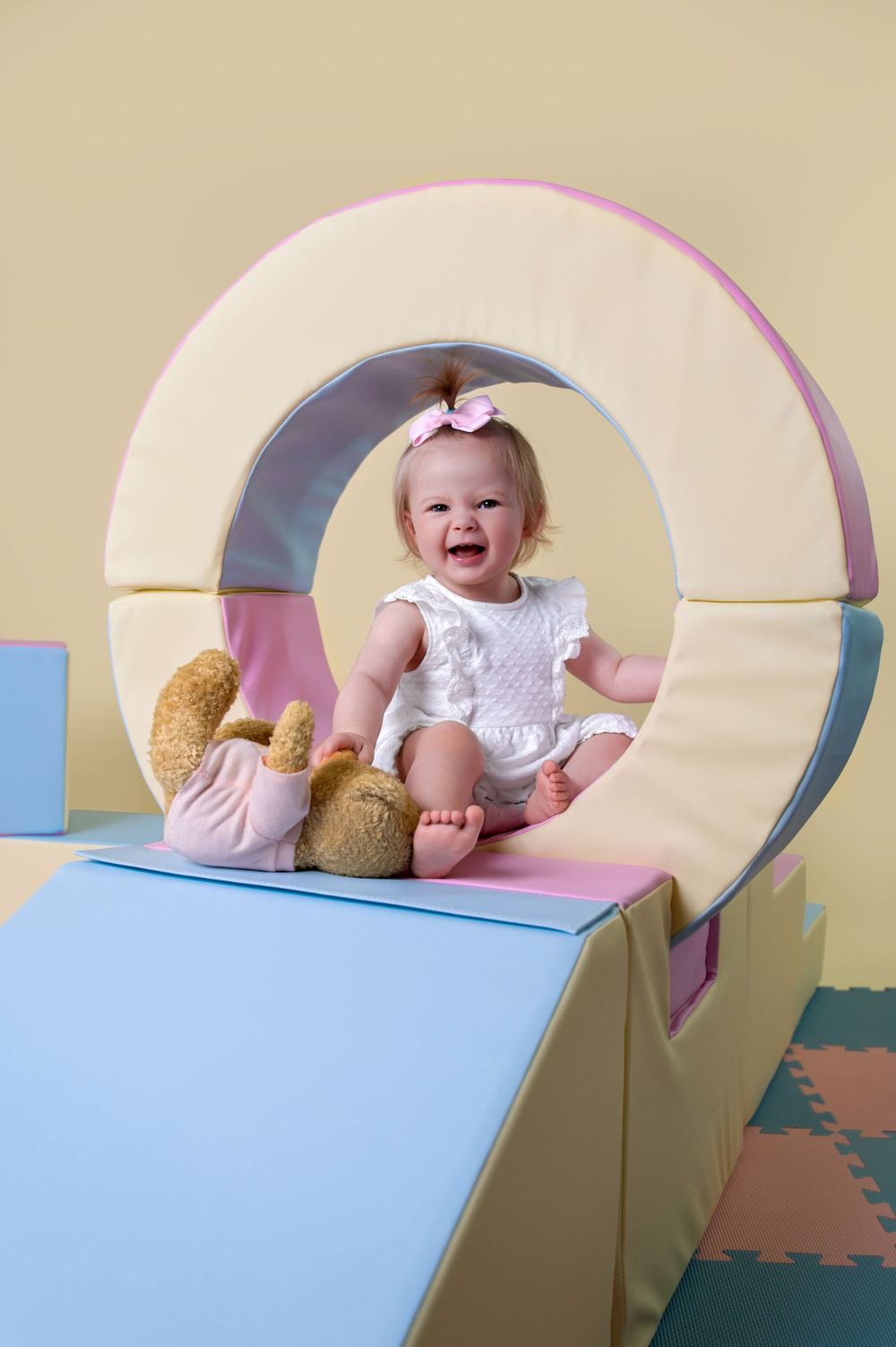 Progression of a baby taking a nap to waking up with a smile in a curved play area with blue and pink colors.