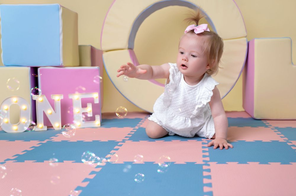 Small child crawls on pink and blue puzzle play mat while exploring.