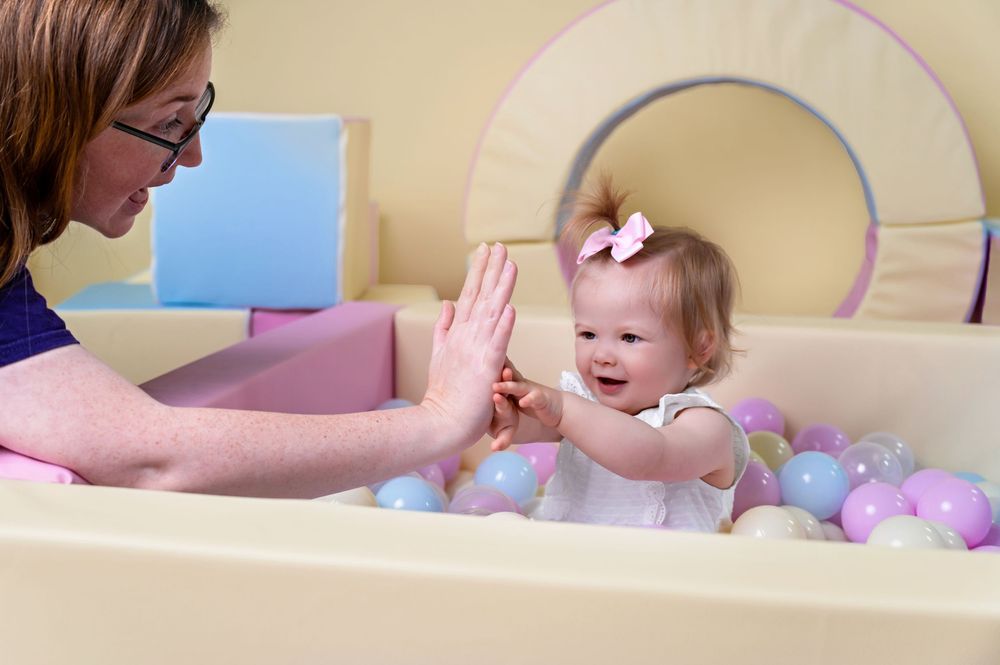 Adult and baby playing together with colorful balls in play area.