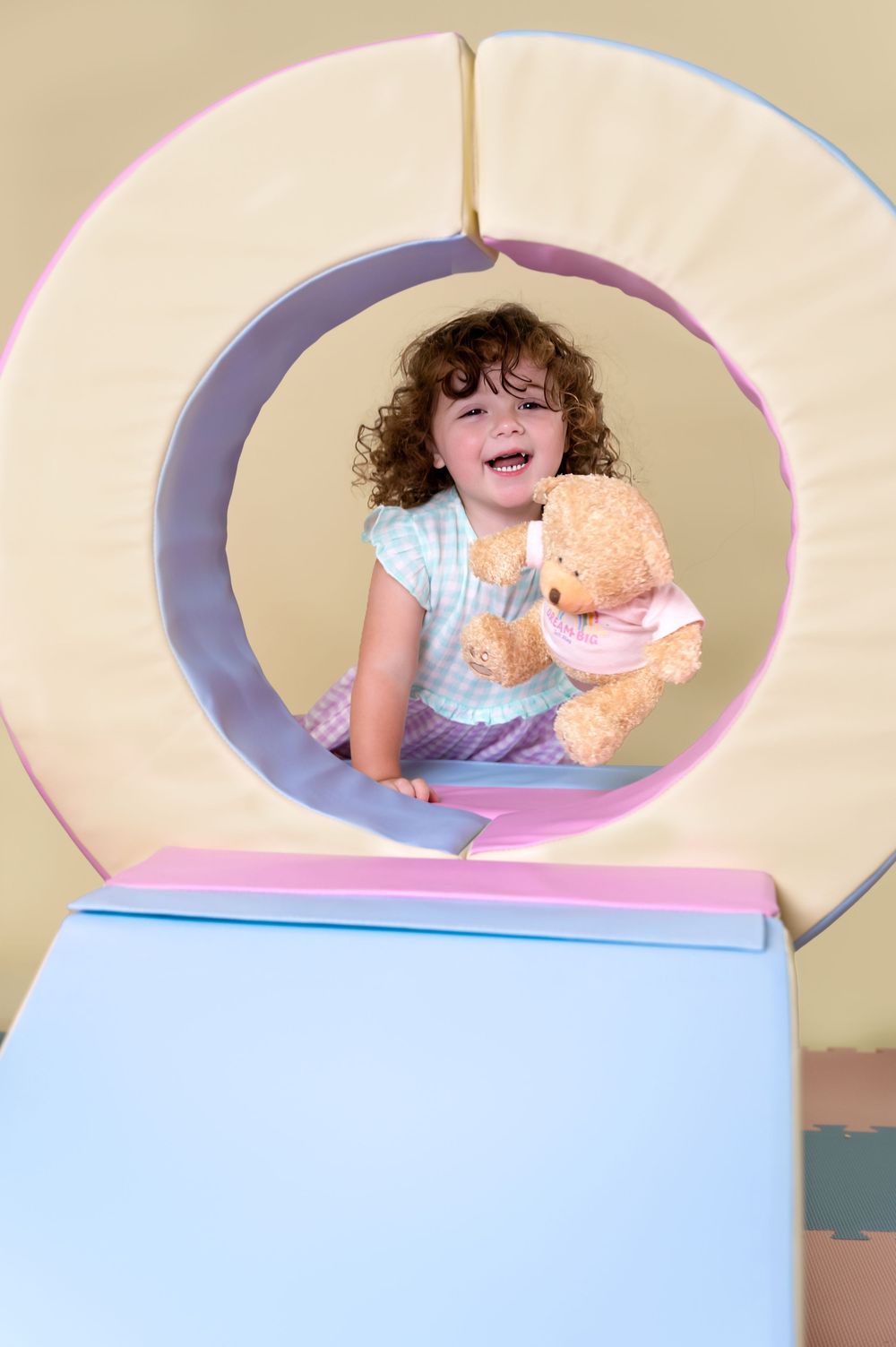 Baby playfully peeks through a round opening in a pastel-colored display setup.
