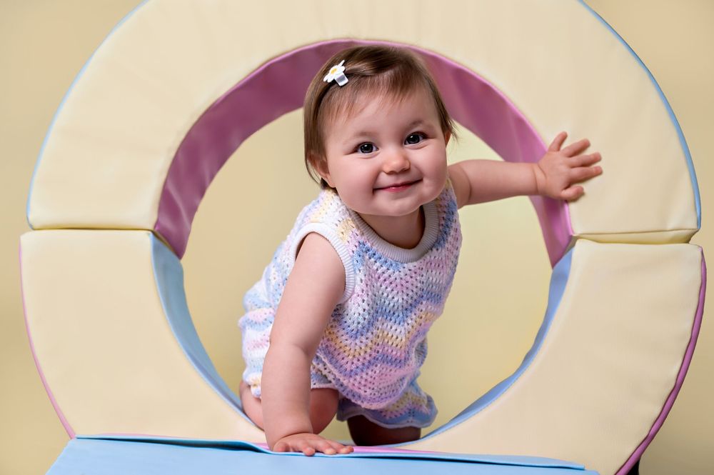 Happy toddler in a polka dot outfit crawls through a colorful circular play tunnel during playtime.
