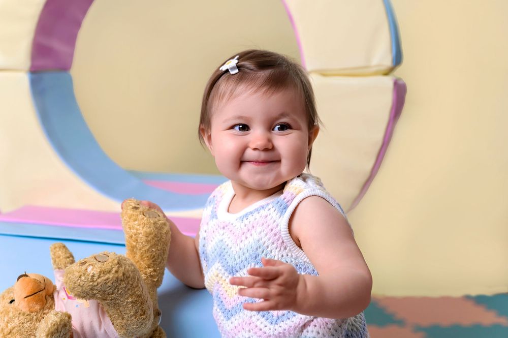 Small child in polka dot outfit smiles while playing with toys against colorful circular backdrop.