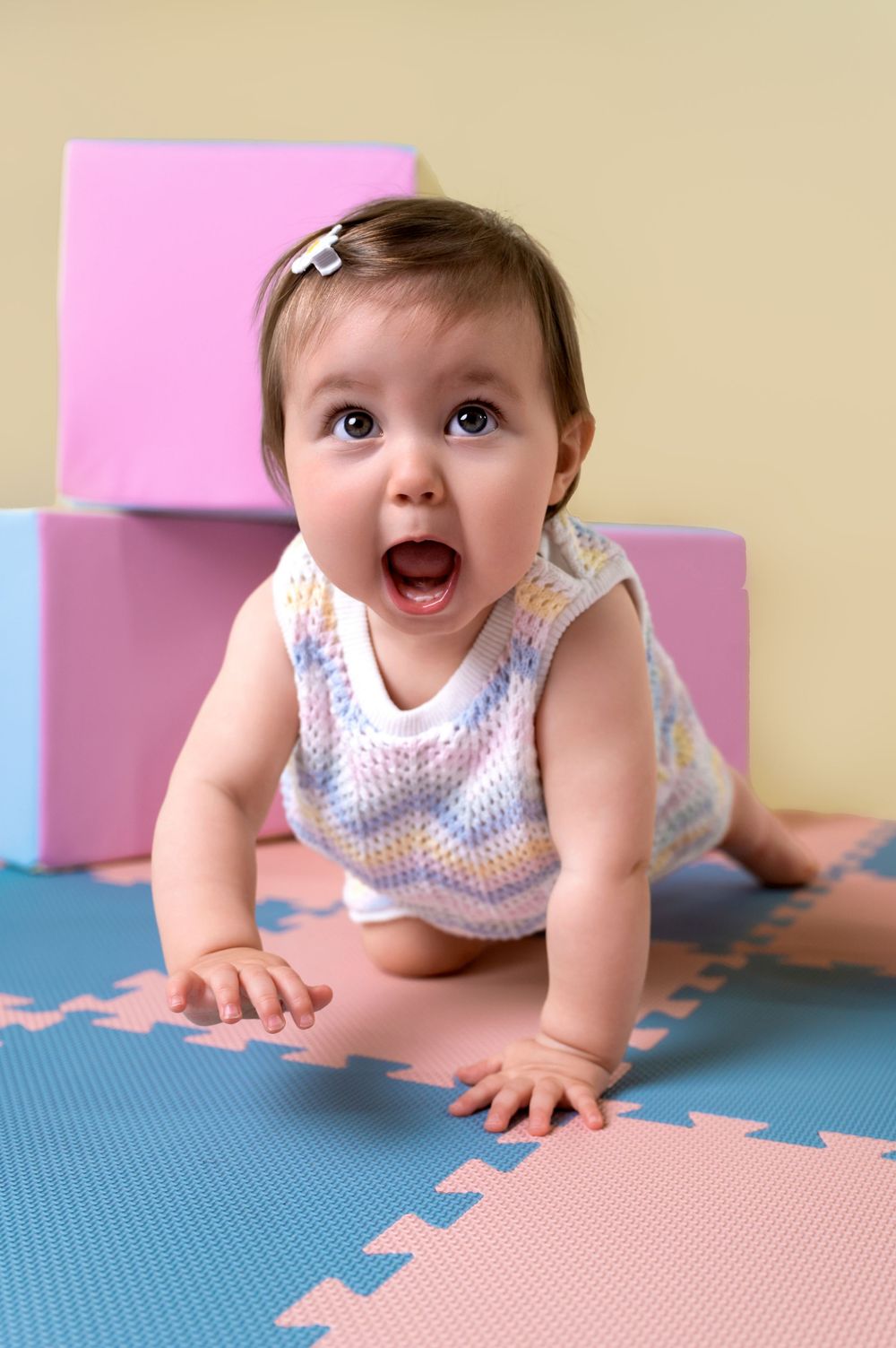 Baby in a knit tank top shows excitement while crawling on pink and blue foam play mats.